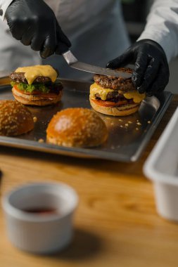 Şef leziz bir hamburger hazırlıyor. Profesyonel mutfak burgeri, etli peynirli, domatesli, kızarmış salatalı.
