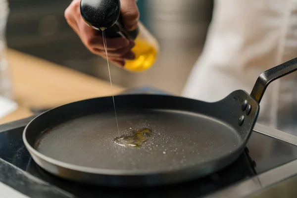 シェフがレストランでプロのキッチン料理で熱い鍋に油を注ぐ — ストック写真