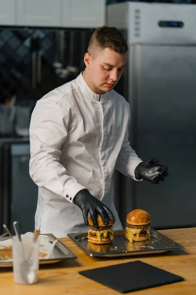 シェフは牛肉パティチーズトマト揚げパンレタスとおいしいハンバーガーのプロのキッチンバーガーを準備します — ストック写真