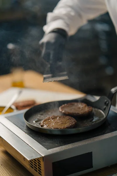 黒手袋のシェフがヘラのプロのキッチンとホットパンの上においしいハンバーガーのパテを反転 — ストック写真