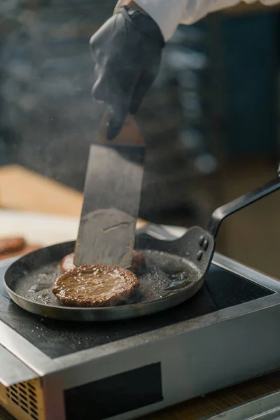 黒手袋のシェフがヘラのプロのキッチンとホットパンの上においしいハンバーガーのパテを反転 — ストック写真