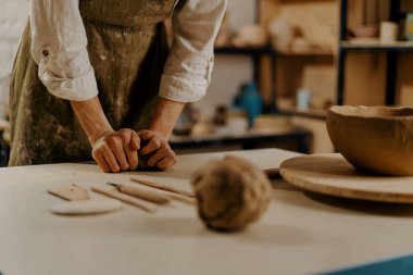 Çömlek atölyesi ustası elleri masada aletlerin arasında killeri yoğurur.