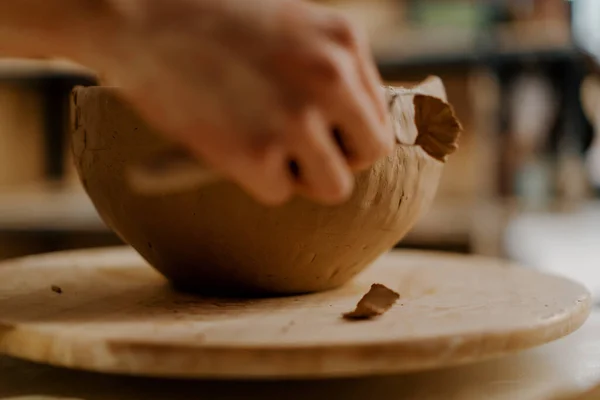 In the pottery workshop the master processes the product with loop for clay sculpts clay dishes on table