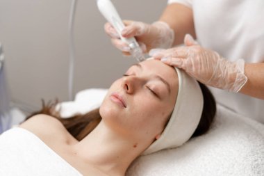 Eldivenli güzellik uzmanı, kozmetoloji kliniğinde cilt bakımı ve cilt temizliği yapıyor. Modern insanlar için profesyonel nemlendirici ve gençleştirici donanım prosedürleri uyguluyor.