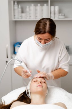 Eldivenli güzellik uzmanı, kozmetoloji kliniğinde cilt bakımı ve cilt temizliği yapıyor. Modern insanlar için profesyonel nemlendirici ve gençleştirici donanım prosedürleri uyguluyor.
