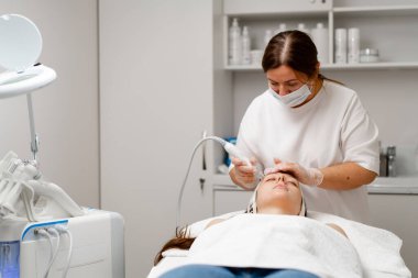 Eldivenli güzellik uzmanı, kozmetoloji kliniğinde cilt bakımı ve cilt temizliği yapıyor. Modern insanlar için profesyonel nemlendirici ve gençleştirici donanım prosedürleri uyguluyor.