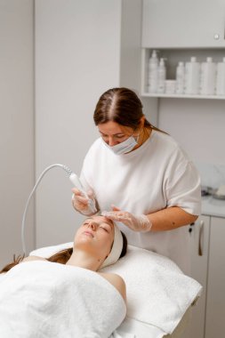 Eldivenli güzellik uzmanı, kozmetoloji kliniğinde cilt bakımı ve cilt temizliği yapıyor. Modern insanlar için profesyonel nemlendirici ve gençleştirici donanım prosedürleri uyguluyor.