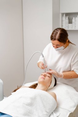 Eldivenli güzellik uzmanı, kozmetoloji kliniğinde cilt bakımı ve cilt temizliği yapıyor. Modern insanlar için profesyonel nemlendirici ve gençleştirici donanım prosedürleri uyguluyor.