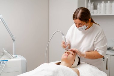 Eldivenli güzellik uzmanı, kozmetoloji kliniğinde cilt bakımı ve cilt temizliği yapıyor. Modern insanlar için profesyonel nemlendirici ve gençleştirici donanım prosedürleri uyguluyor.