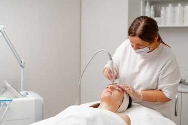 Eldivenli güzellik uzmanı, kozmetoloji kliniğinde cilt bakımı ve cilt temizliği yapıyor. Modern insanlar için profesyonel nemlendirici ve gençleştirici donanım prosedürleri uyguluyor.