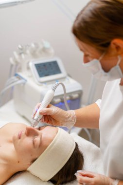 Eldivenli güzellik uzmanı, kozmetoloji kliniğinde cilt bakımı ve cilt temizliği yapıyor. Modern insanlar için profesyonel nemlendirici ve gençleştirici donanım prosedürleri uyguluyor.