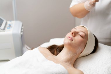 Güzellik salonundaki bir maskeyle yüz bakımı yapan bir kadın kozmetik ürün jeli soyma maskesiyle güzellik kliniğinde müşteri cilt bakımı ve kozmetik spa konsepti için profesyonel maske takıyor.