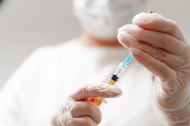 Arka plandaki tıp bürosuna enjeksiyon için şırınga tutan kadın doktorun elleri. Kozmetoloji enjeksiyonu kavramı.