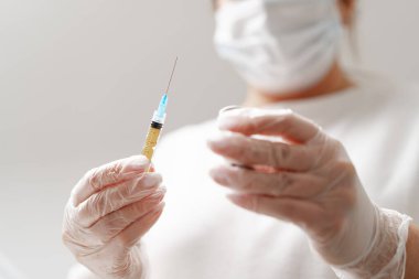 Arka plandaki tıp bürosuna enjeksiyon için şırınga tutan kadın doktorun elleri. Kozmetoloji enjeksiyonu kavramı.