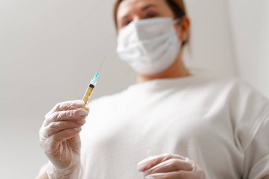 Arka plandaki tıp bürosuna enjeksiyon için şırınga tutan kadın doktorun elleri. Kozmetoloji enjeksiyonu kavramı.