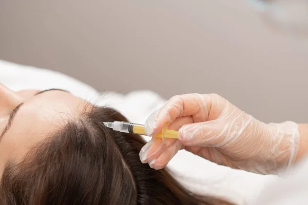 A beautician makes injections into the scalp for hair growth Mesotherapy for hair growth and strengthening in beauty salon A procedure against hair loss