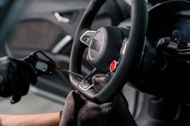 Eldivenli bir tamirci direksiyonu mikrofiber bezle temizler ve özel aletle toz üfler.