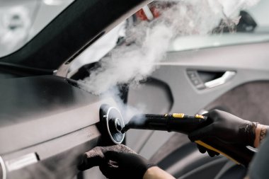 Araba temizleme ve temizleme konsepti. Detaylı temizlik ustası arabanın içini sıcak bir buhar temizleyicisiyle temizliyor.