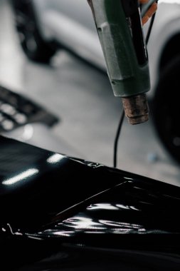 Bir işçi, atölyede saç kurutma makinesi ve kapanış spatulayla araba temizliği ve bakımı ile bir film ile bir araba spoiler kaplar