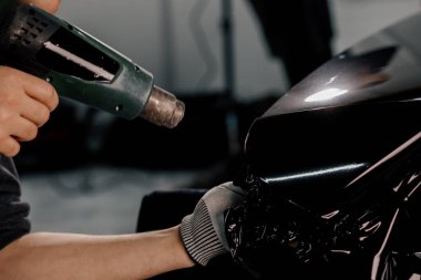 Bir işçi, atölyede saç kurutma makinesi ve kapanış spatulayla araba temizliği ve bakımı ile bir film ile bir araba spoiler kaplar
