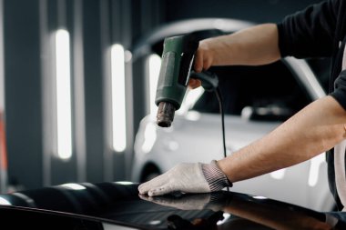 Bir işçi, atölyede saç kurutma makinesi ve kapanış spatulayla araba temizliği ve bakımı ile bir film ile bir araba spoiler kaplar