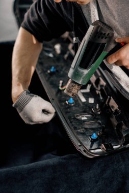 Bir işçi, atölyede saç kurutma makinesi ve kapanış spatulayla araba temizliği ve bakımı ile bir film ile bir araba spoiler kaplar