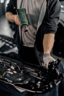 Bir işçi, atölyede saç kurutma makinesi ve kapanış spatulayla araba temizliği ve bakımı ile bir film ile bir araba spoiler kaplar