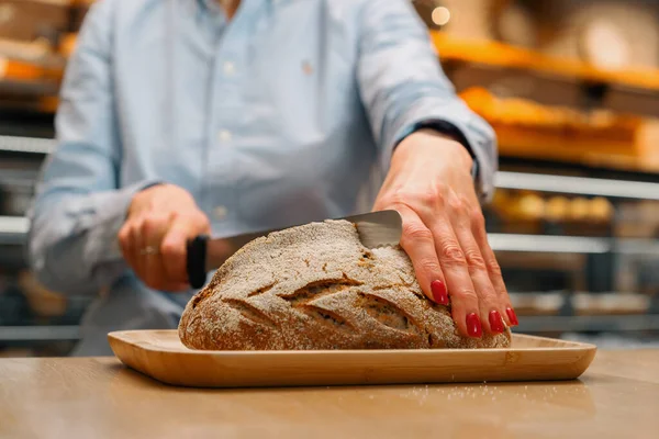 bakery - woman baker cuts freshly baked dark bread