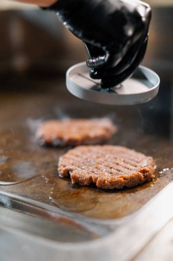 Restoranın mutfağındaki aşçı hamburgerler için pirzola yapar burgerleri ezer biftekleri ezer
