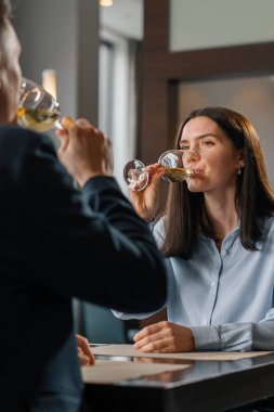 Bir otel restoranında bir adam ve bir kadın gülümseyen bir kızın yüzünde beyaz şarap içerler.