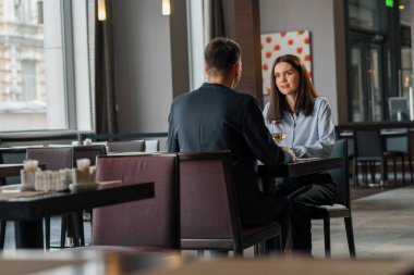 Bir otel restoranında bir adam ve bir kadın gülümseyen bir kızın yüzünde beyaz şarap içerler.
