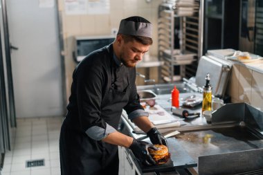 Otel restoranında profesyonel mutfak. Şef hamburgerin malzemelerini hazırlıyor.