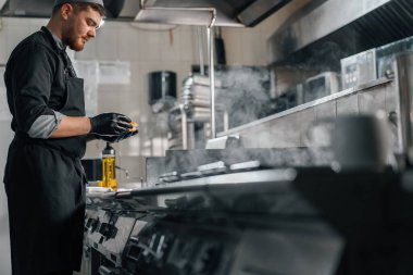Otel restoranındaki profesyonel mutfak aşçısı ızgaraya hamburgerli çörek koyar.