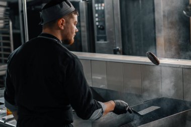 Otel restoranında profesyonel bir mutfak. Şef havada spatulayla hamburger köftesi çeviriyor.