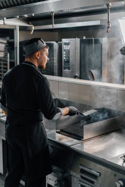 Otel restoranında profesyonel bir mutfak. Şef havada spatulayla hamburger köftesi çeviriyor.