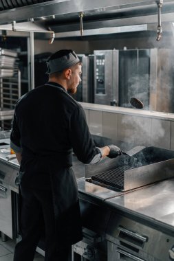 Otel restoranında profesyonel bir mutfak. Şef havada spatulayla hamburger köftesi çeviriyor.