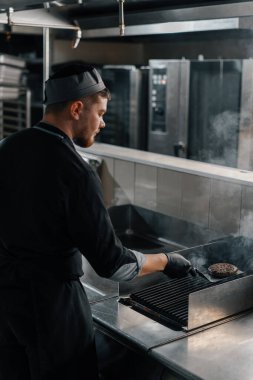 Otel restoranındaki profesyonel mutfak şefi hamburgerin üstünde köfte pişiriyor.