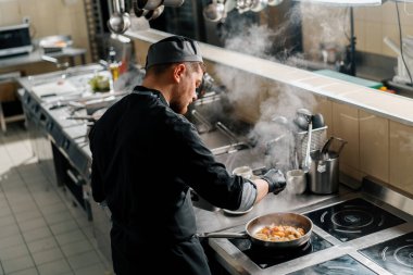 Otel restoranında profesyonel mutfak. Şef tavada deniz ürünleri kızartıyor.