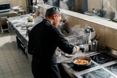 Otel restoranında profesyonel mutfak. Şef tavada deniz ürünleri kızartıyor.