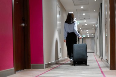 Elinde bavul olan bir kız, seyahat sırasında otel koridorunda bir iş kadınının dikiz aynasından yürür.