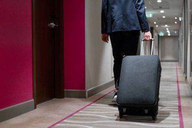 Elinde bavul olan bir adam otel koridorunda yürürken bir iş adamının yolculuktaki arka görüntüsü.