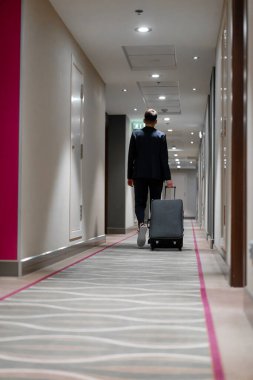 Elinde bavul olan bir adam otel koridorunda yürürken bir iş adamının yolculuktaki arka görüntüsü.