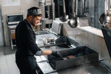 Otel restoranındaki profesyonel mutfak şefi hamburgerin üstünde köfte pişiriyor.