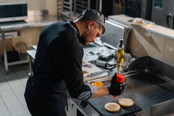 ホテルのレストランでプロのキッチンシェフはハンバーガー用のパンにソースを塗り — ストック写真