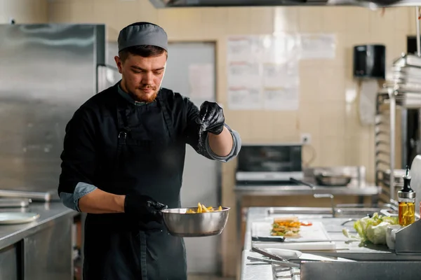 饭店餐厅的专业厨房厨师正在给美味的薯条加盐 — 图库照片