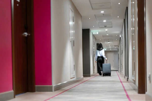 A girl with a suitcase walks down the hotel corridor rear view of a business woman during trip