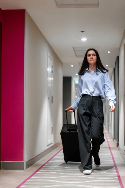 A girl with a suitcase walks down the corridor of hotel  businesswoman on trip the concept of travel