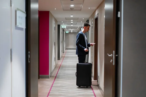 Elinde bavul olan bir adam otel odasının kapısını açıyor. Seyahat konsepti olan bir iş adamı.