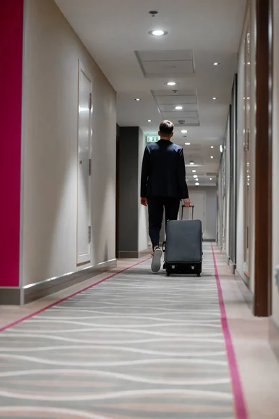 A man with a suitcase walks down the hotel corridor a back view of a businessman on trip