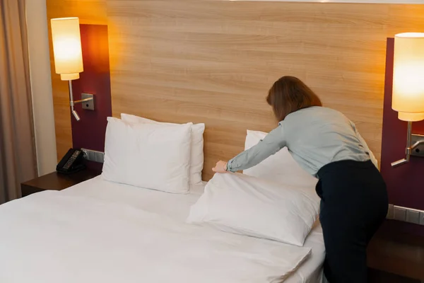 A housekeeper in a uniform makes a bed preparing luxury hotel room for guests cleaning and travel concept